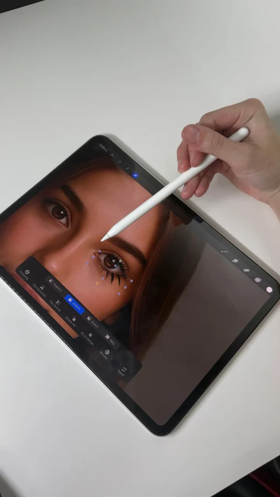 A tablet screen showing a close up of an eye being digitally edited with an Apple Pencil, focusing on detailed lash design work to illustrate different lash extension styles.